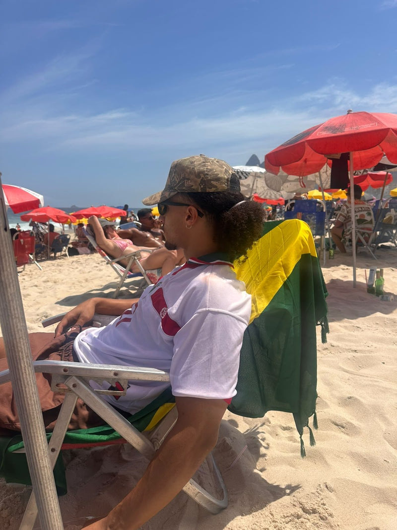 Personne en maillot REALAW DROP 01 blanc et rouge assise sur une chaise de plage, parasols rouges derrière